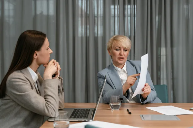 Two businesswomen discussing documents during a professional meeting around a conference table. Lönesamtalet som ger resultat: förberedelse, argument och uppföljning